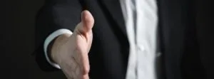 A businessman in a suit extending his hand for a handshake, symbolizing professionalism, trust, and welcoming service in real estate or business interactions.